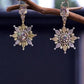 IXXIA Jewelry radiant starburst drop earrings with gold and silver tones, clear gemstones, and rectangular stud top. 